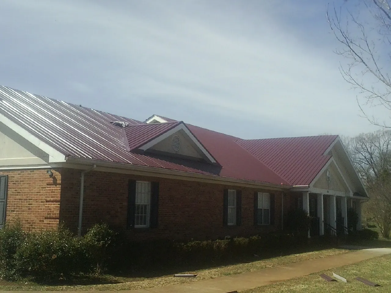 Red metal roof with gabled entries on a long brick building, from a Hail Damage Roof Repair job in Monongahela