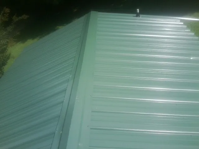 New green metal panels meeting at the ridge of a roof — Flat Roof Repair work by our crew in Monongahela