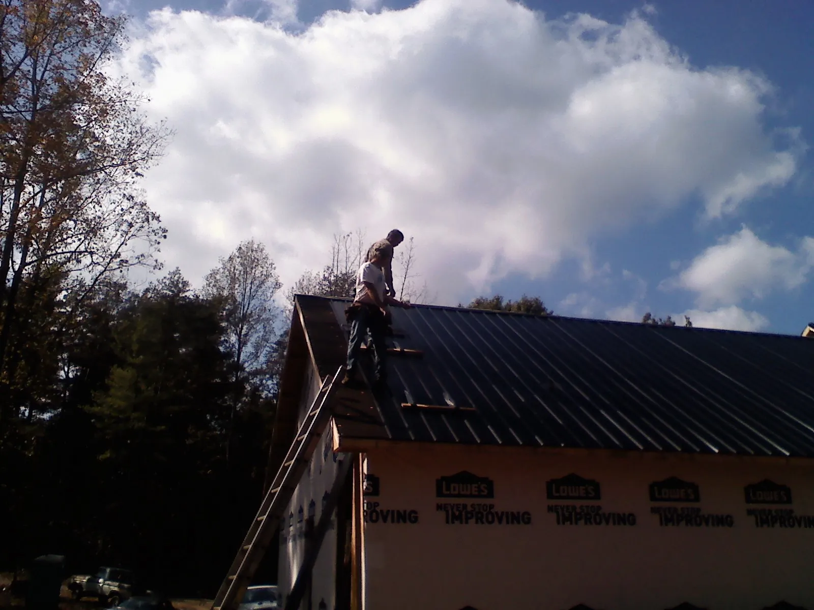 Roofer fastening dark metal panels high against a cloudy sky, from a Roof Inspection job in Monongahela