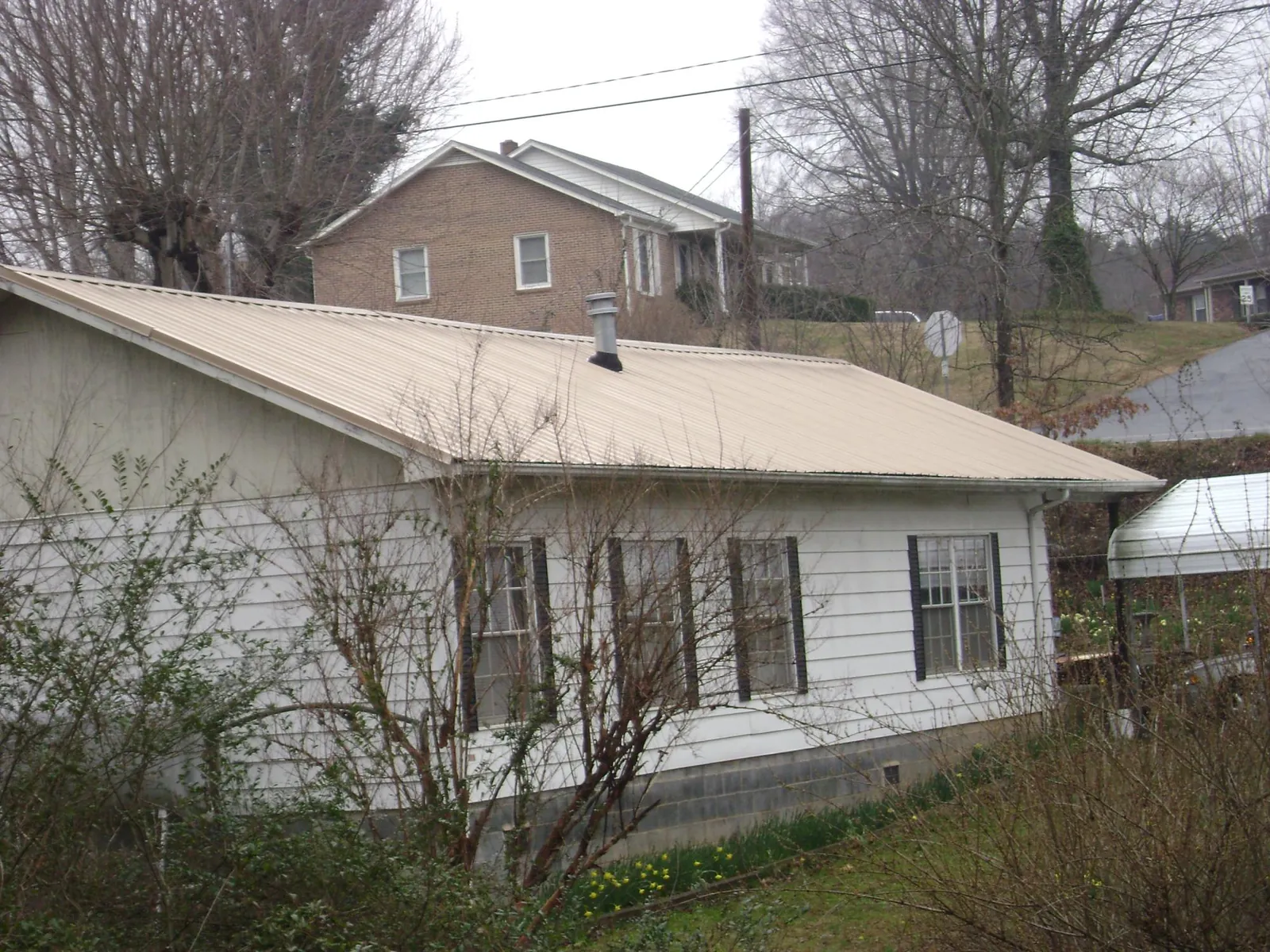 Tan metal roof on a white sided house set into a hillside — Commercial Roofing by Roofing Brothers in Monongahela